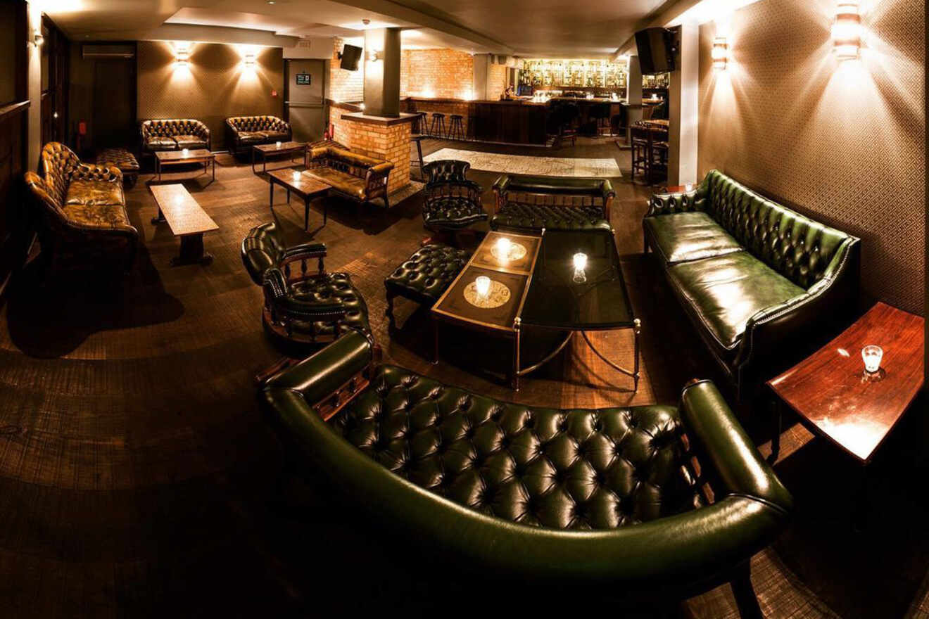 A spacious lounge bar with tufted green leather sofas, dim lighting, and low tables creating an intimate and relaxed atmosphere.