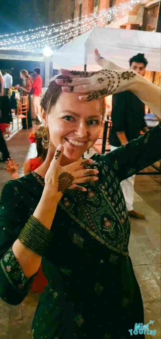 The writer of the post posing with intricate mehndi designs on her hands at an event, with string lights and guests in the background.