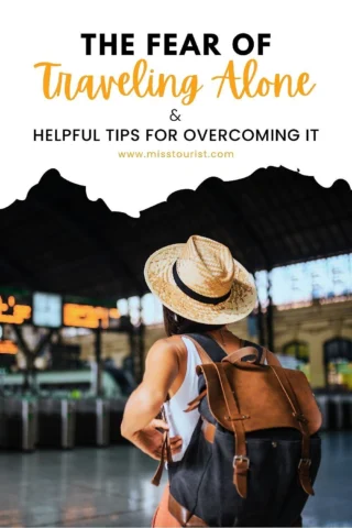 A person with a hat and backpack stands inside a train station. The text on the image reads, "The Fear of Traveling Alone & Helpful Tips for Overcoming It. www.misstourist.com.