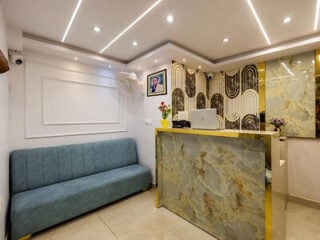 Reception area at Hotel All In Homes near New Delhi Railway Station, with a marble-effect front desk, gold trim and a teal sofa.