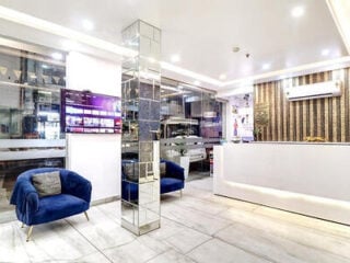 Lobby at Hotel Emporio Dx in Paharganj, New Delhi, with blue velvet armchairs, a mirrored column and a white reception desk.