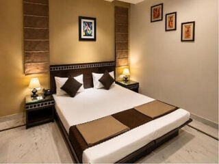 Double room at Smyle Inn near New Delhi Railway Station, with a beige and brown bed runner, matching bedside lamps and framed artwork on the walls.