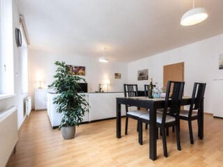 Modern dining and living area with black dining table, four chairs, white sofa, indoor plant, wooden floor, and two pendant lights.
