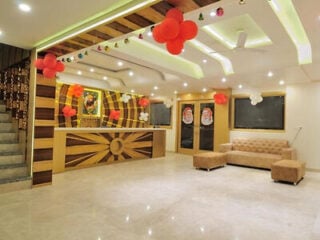 Lobby at The Gold Inn in Paharganj, New Delhi, with a decorative wooden reception desk, beige sofa and red balloon decorations on the ceiling.