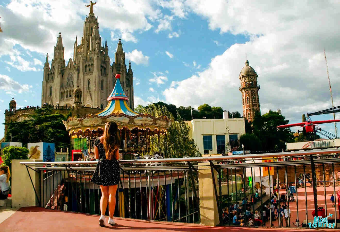 author of the post stands on a balcony overlooking an amusement park with a decorative building and a tall church in the background.