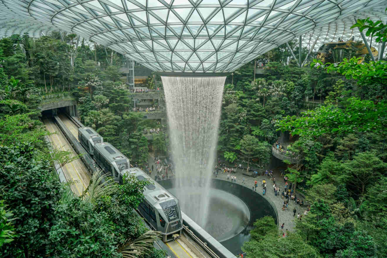 Indoor waterfall and train at Jewel Changi Airport, Singapore, surrounded by lush greenery under a glass dome.