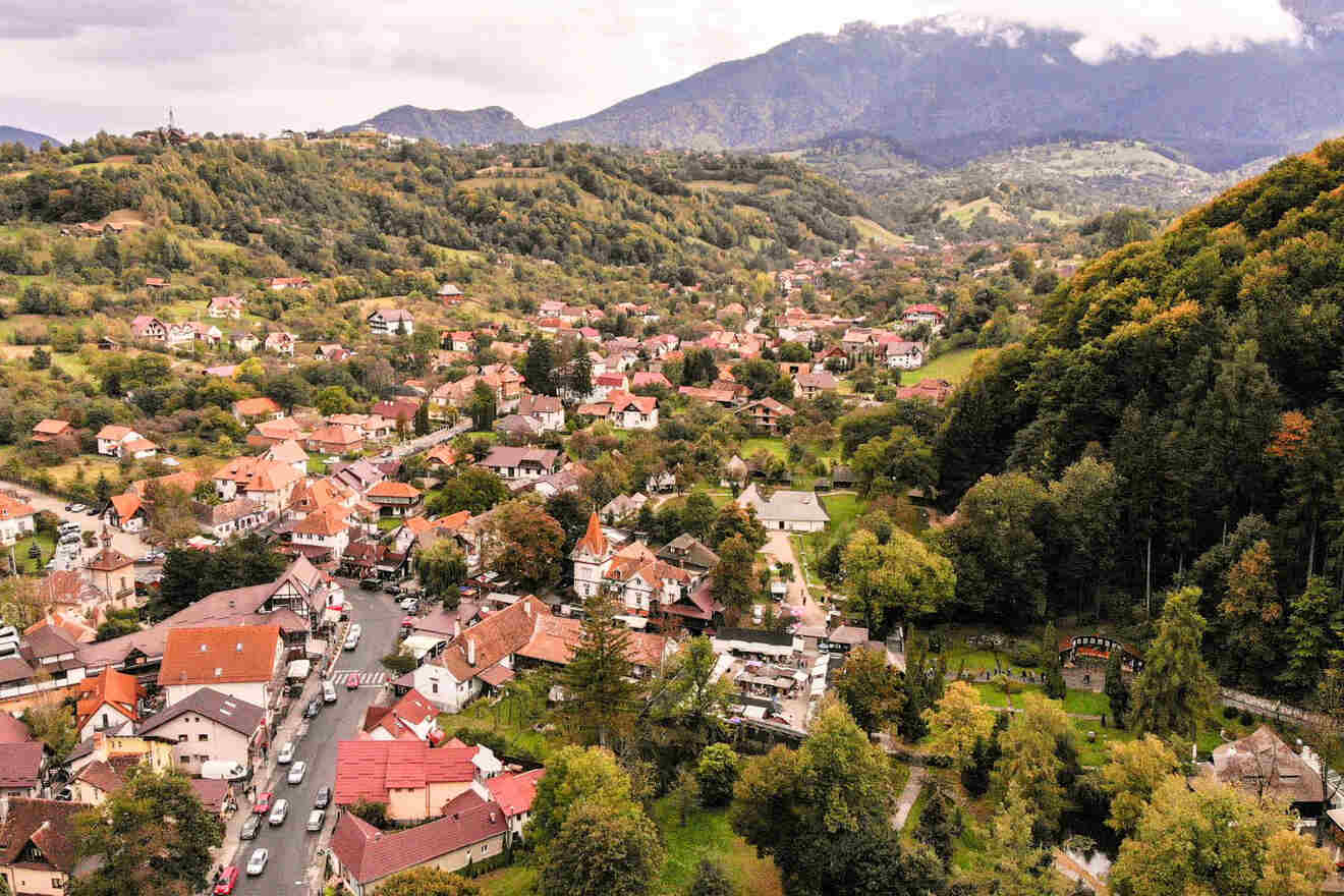 Aerial view of a small town with red-roofed buildings nestled among green hills and mountains in the background.