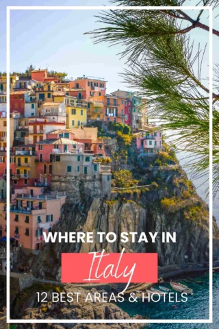 Colorful buildings perched on a rocky cliffside by the sea, with text overlay "Where to Stay in Italy: 12 Best Areas & Hotels." Pine tree branches frame the right side of the image.