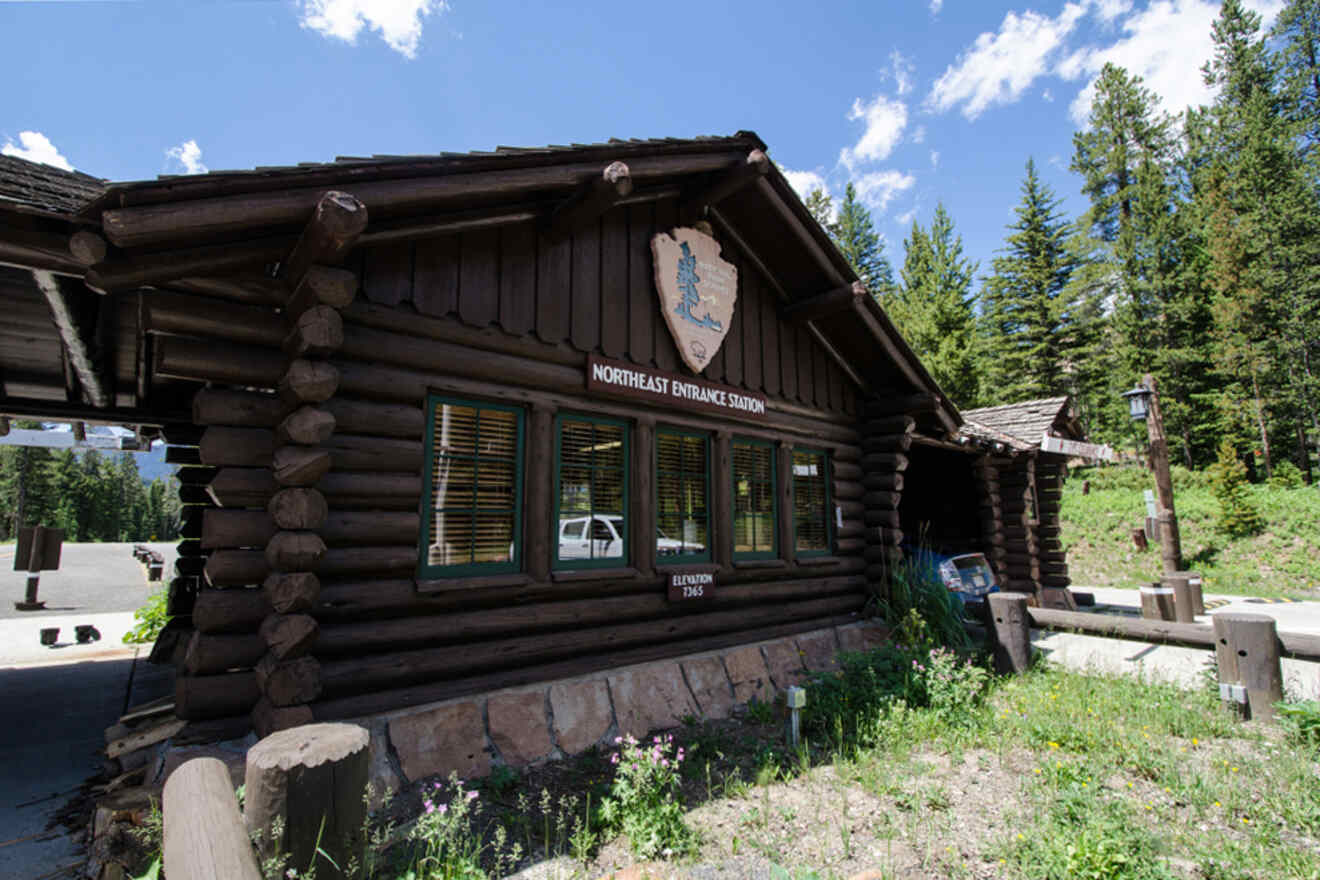 Log cabin labeled "Northeast Entrance Station" with a forest and partly cloudy sky in the background.