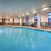 Indoor swimming pool with clear water, lined by blue chairs and large windows.
