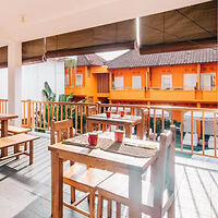 A sunny outdoor dining area with wooden tables and chairs, overlooking a building with bright orange walls.