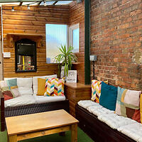 Cozy room with two cushioned sofas, a wooden coffee table, colorful pillows, a potted plant, and a mirror on a brick and wooden wall.