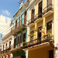 Colorful colonial-style buildings with balconies line a street under a clear blue sky.