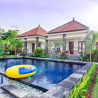 View of a serene outdoor pool with a yellow inflatable raft, surrounded by tropical landscaping and a villa-style house with red-tiled roofs in the background.