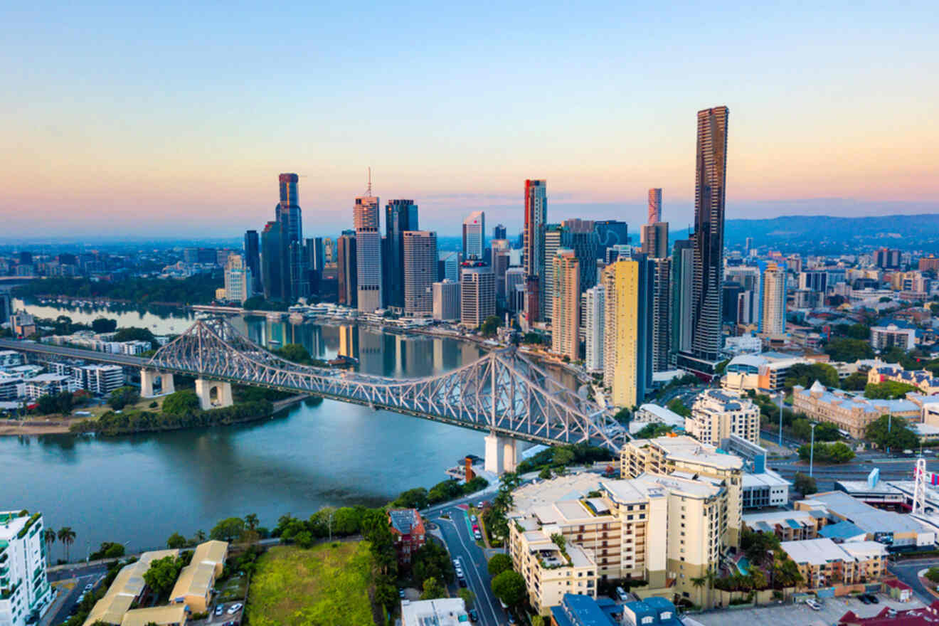 Aerial view of a city skyline with a large bridge spanning a river, surrounded by tall buildings under a clear sky.