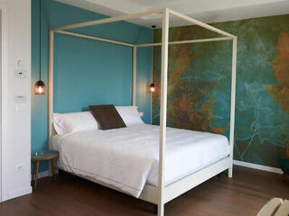 A modern bedroom with a four-poster bed, teal accent wall, pendant lights, and a round bedside table.