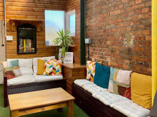 Cozy room with brick and wood walls, featuring two cushioned sofas with colorful pillows, a small wooden table, and a potted plant.