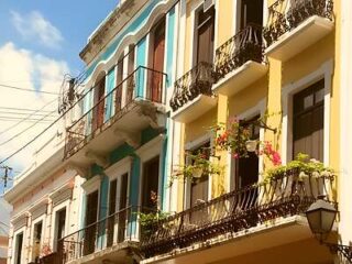 Colorful colonial-style buildings with balconies and plants under a blue sky.