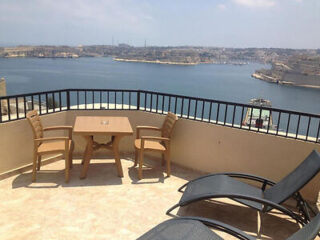 Terrace with table, chairs, and loungers overlooking a body of water and distant land.