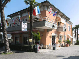 A two-story hotel with flags of different countries on the balcony. The building is peach-colored with outdoor seating and surrounded by palm trees.