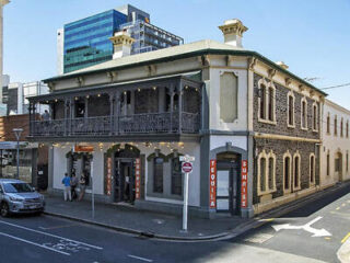 Historic two-story corner building with a balcony, stone facade, and signage for "Tequila Sunset." Urban setting with a parked car and a few people near the entrance.