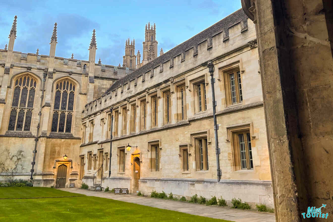 Historic stone building with pointed arches and spires, featuring a courtyard with a well-maintained lawn and stone path.