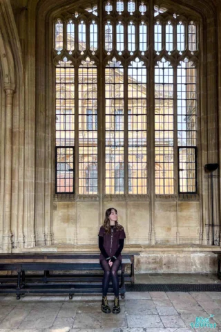 author of the post sits on a bench in front of tall, arched windows with detailed stonework.