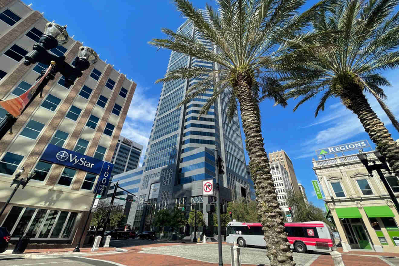 Street view of a city with a tall, striped building, palm trees, a bank sign, and a bus.