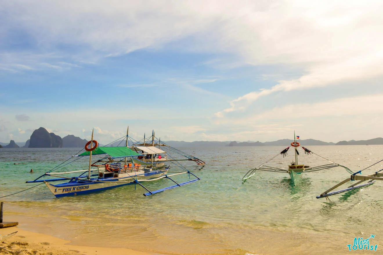 Boats anchored on a sandy beach with a clear sky and distant islands in the background.