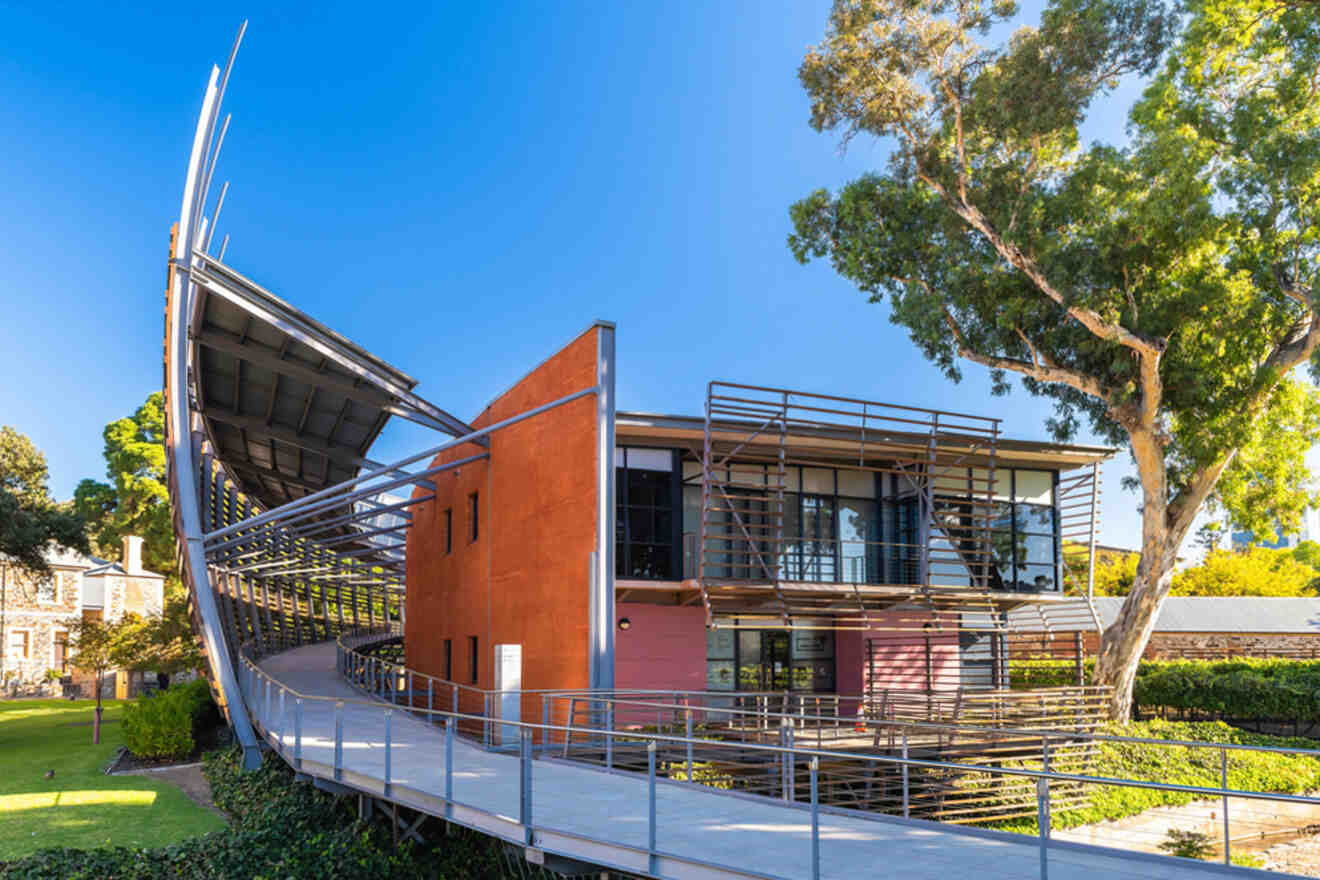 Modern building with a curved ramp and large windows, set among trees against a clear blue sky.