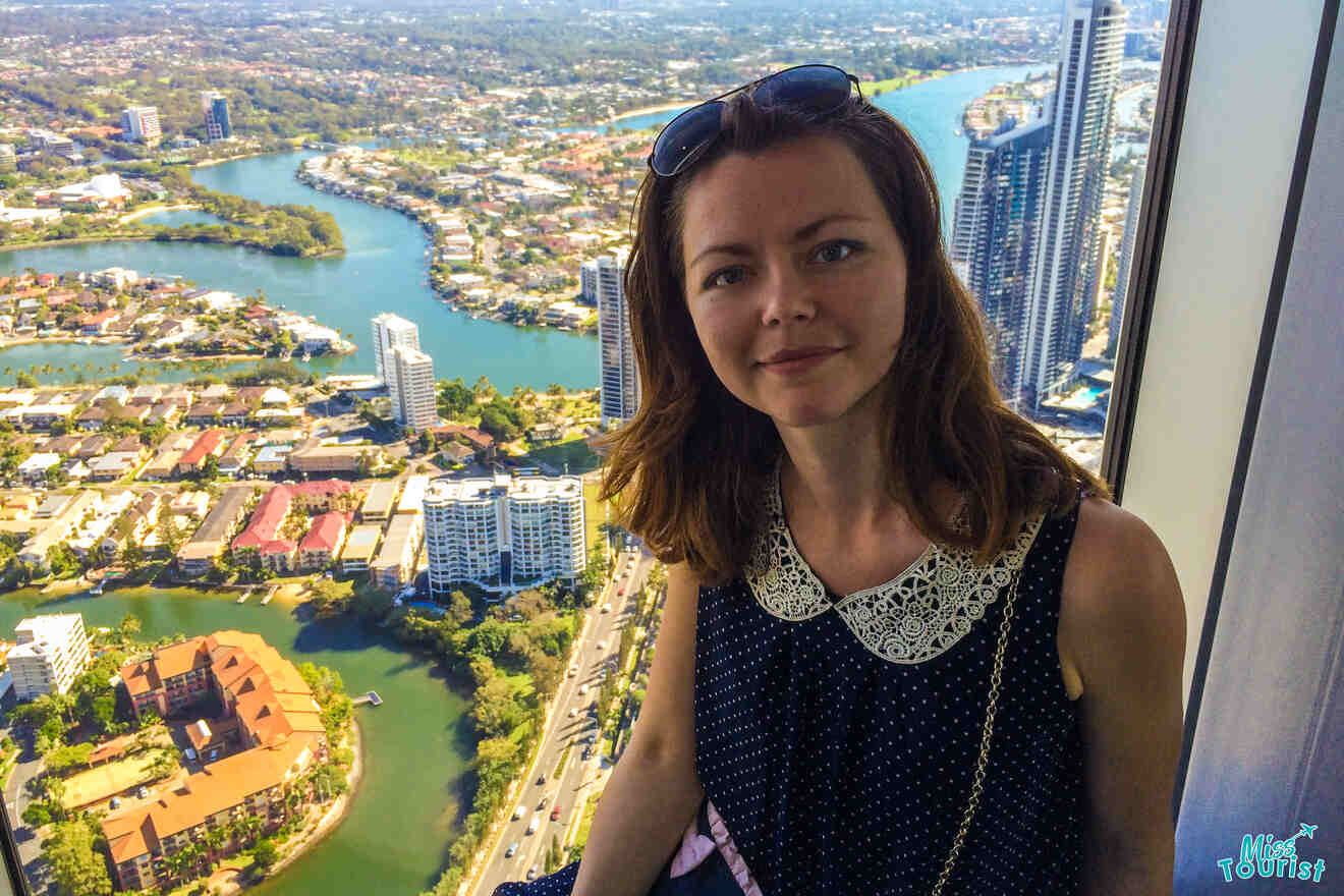 author of the post standing in front of a window with a view overlooking a cityscape with rivers, tall buildings, and greenery.