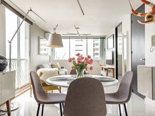 Modern dining area with a round table, tulips centerpiece, four chairs, floor lamps, and large windows providing natural light. A toy hangs from the ceiling.