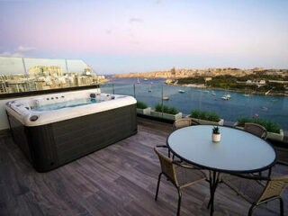 Rooftop terrace with a hot tub and table with chairs overlooking a waterfront view at sunset.