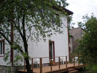 A white two-story house with a wooden deck, white chairs, and a tree in the foreground.