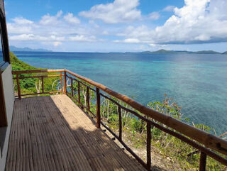 Wooden deck overlooking a clear blue ocean with scattered clouds in the sky and distant islands on the horizon.