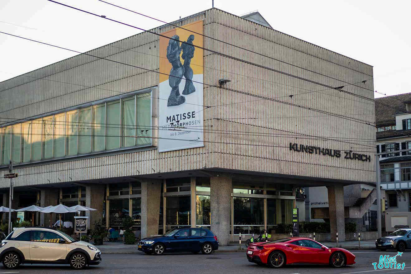 Exterior of Kunsthaus Zürich with a large poster for a Matisse exhibition. Several cars are parked or driving by in the foreground.