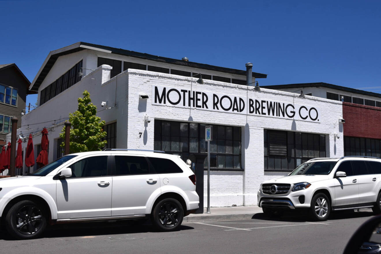 White building labeled "Mother Road Brewing Co." with two white cars parked in front.