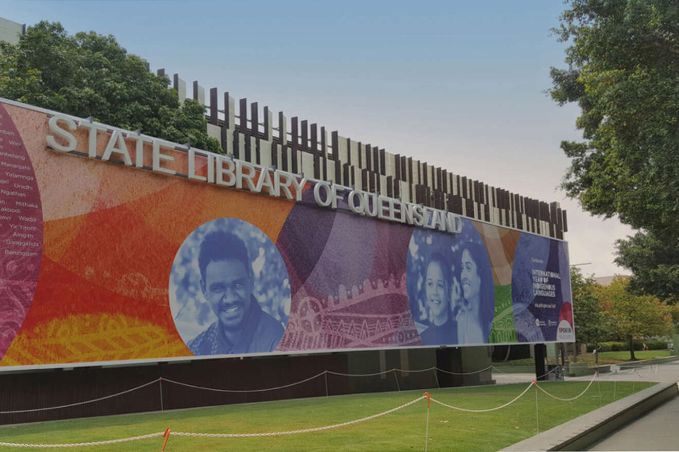 State Library of Queensland building with a large colorful mural featuring smiling people and abstract designs.