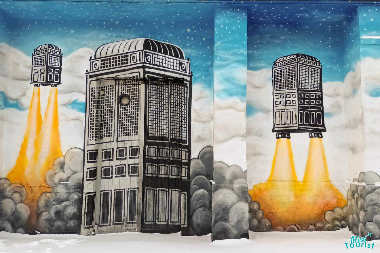 Mural of buildings depicted as rockets launching into a cloudy, blue sky with fiery trails.