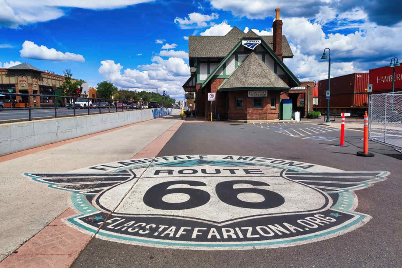 A road with a large "Route 66" emblem in Flagstaff, Arizona, near historic buildings and a clear sky.