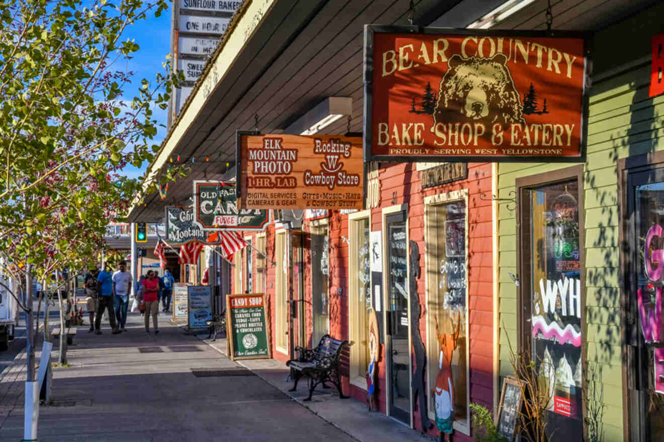 A colorful street with various shops, including a bake shop with a bear sign, a candy store, and a cowboy store. People are walking on the sidewalk.