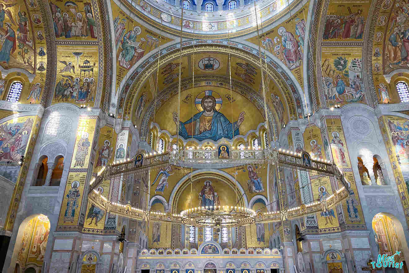 Interior of a richly decorated church with golden mosaics and religious figures on the walls and ceiling, centered by a large depiction of Christ.