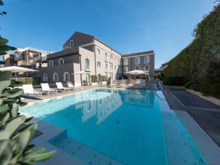 Outdoor swimming pool with lounge chairs, umbrellas, and a building in the background under a clear blue sky.