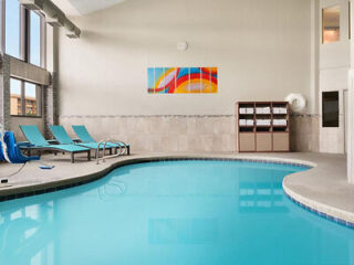 Indoor pool area with abstract artwork on the wall, blue lounge chairs, and a towel rack in the corner.