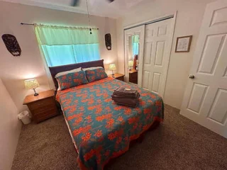 A cozy bedroom with a double bed featuring colorful bedding, two bedside tables with lamps, a mirrored closet, and folded towels on the bed.