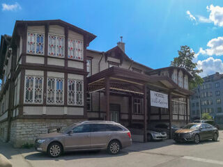 A two-story wooden building with stained glass windows and parked cars in front, featuring a sign that reads "Hostel.