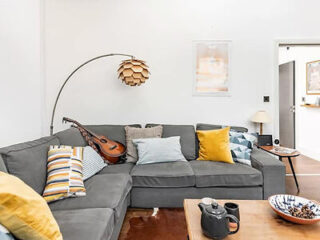 A cozy living room with a gray sectional sofa adorned with multi-colored pillows, a hanging lamp, a mandolin, a wooden coffee table, and various decorations.