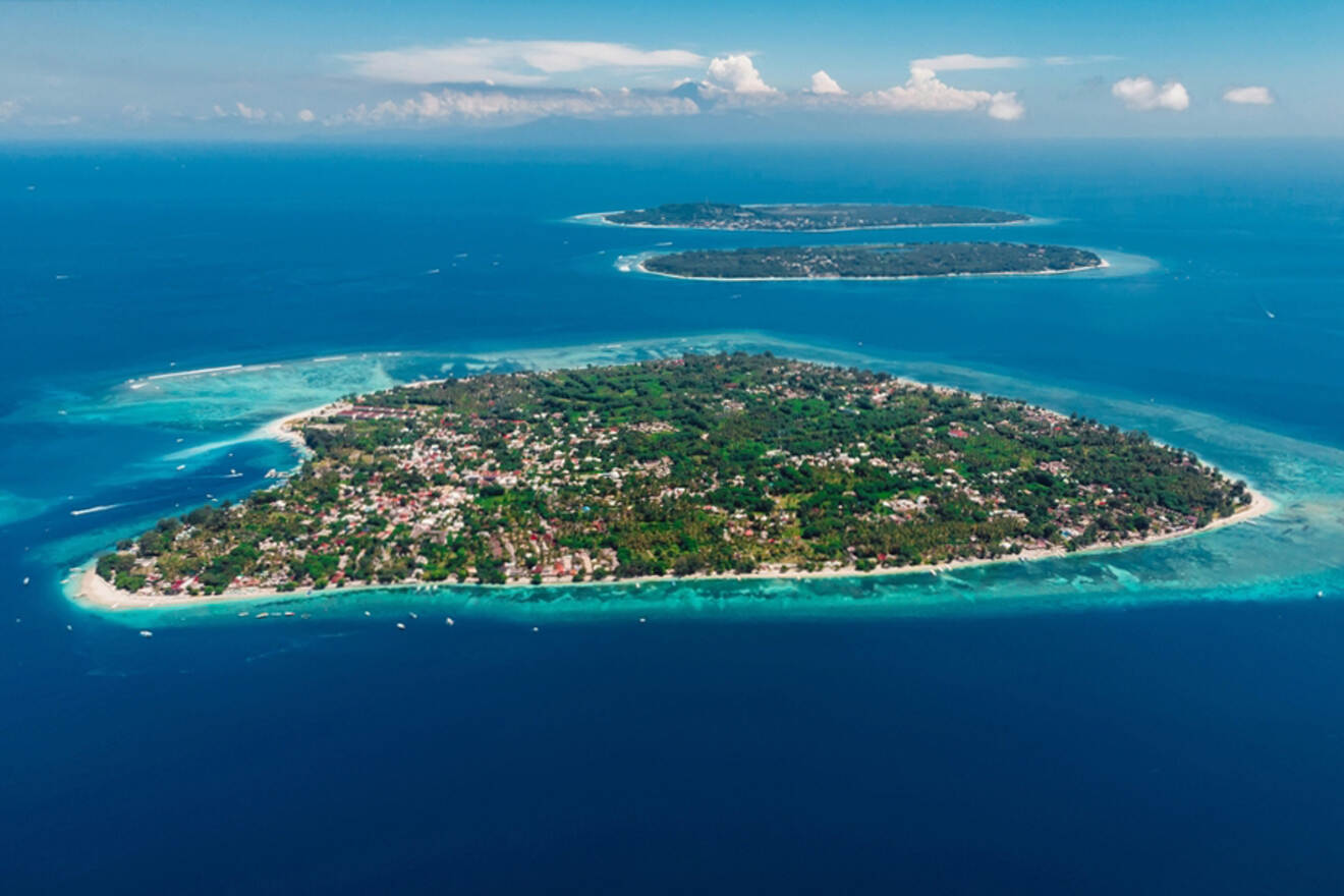 Aerial view of three lush green islands surrounded by clear blue ocean waters and a few scattered clouds in the sky.