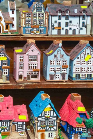 Colorful ceramic model houses are displayed on wooden shelves, each with price tags.