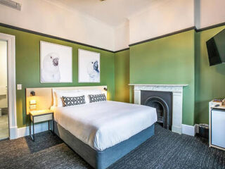 A bedroom with green walls, a double bed, two animal artworks, a fireplace, a wall-mounted TV, and a small fridge.